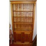 A modern pine freestanding open bookshelf, having twin cupboard lower doors, w.96cm
