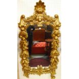 An early 20th century heavy floral and fruit encrusted giltwood framed wall mirror, having scallop