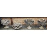 A set of four reconstituted stone pedestal garden urns, each having twin rams head handles, with