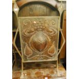 An Art Nouveau embossed and floral stylised copper inset fire screen, raised in an angular steel