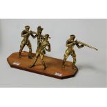 A brass sculpture modelled as a huntsmen and two soldiers on teak plinth, plinth width 35cm