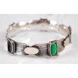 An Arts & Crafts bangle, the 12mm wide textured bangle set with oval collet mounted green enamel