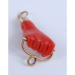 A carved coral pendant in the form of a closed fist holding two yellow looped bar, length 25mm,
