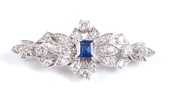 A white metal Art Deco style lozenge shaped brooch, featuring a centre square cut sapphire within