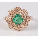 A yellow metal, emerald and diamond circular cluster ring, the round emerald within an interwoven