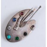 A white metal brooch in the form of an artist's pallet , set with tourmaline, green garnet,