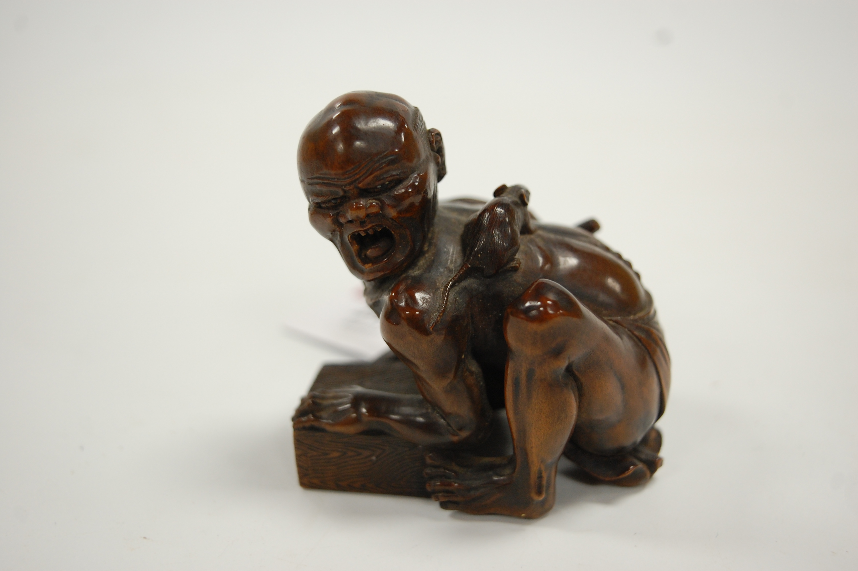 A Japanese Meiji period softwood netsuke, carved as a man in kneeling pose with rat upon his back,