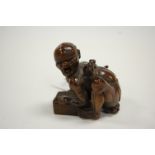 A Japanese Meiji period softwood netsuke, carved as a man in kneeling pose with rat upon his back,