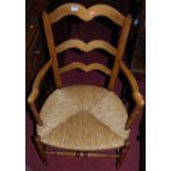 An early 20th century beech ladder back rush seat elbow chair, together with a further ladder back