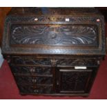 A circa 1900 ebonised and heavily relief carved oak slopefront writing bureau, having an arrangement