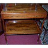 A reproduction yew wood two-tier side table, having single frieze drawer raised on brass roller