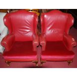 A pair of early 20th century walnut framed and red rexine studded upholstered wingback armchairs,