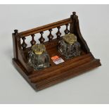 A late Victorian oak desk stand having a spindle back and twin glass inkwells each with brass