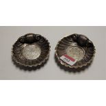 A pair of white metal scallop shaped dishes each inset with a Maltese coin