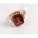 A yellow metal garnet set dress ring, the emerald cut garnet flanked to either side by a pair of