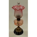 A Victorian pedestal oil lamp having cranberry tinted etched frilled glass shade above a pink tinted