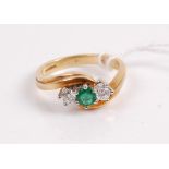 A contemporary 18ct gold emerald and diamond three stone ring, the round cut emerald flanked with