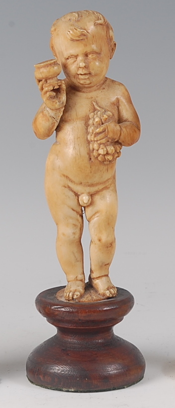 A 19th century continental carved ivory figure of a standing nude boy, holding a bunch of grapes and