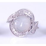 A white metal carved 'man in the moon' moonstone and diamond ring, the centre round moonstone