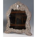 An Edwardian silver and embossed easel dressing table mirror, having a shaped and bevelled plate