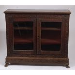 A circa 1900 Burmese heavily carved 'rosewood' double door glazed bookcase, the egg & dart moulded