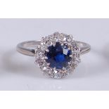 A white metal, sapphire and diamond circular cluster ring, featuring a centre round faceted sapphire