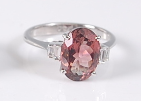 A white metal, pink tourmaline and diamond ring, featuring an oval pink tourmaline in a four-claw