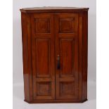 A George III walnut hanging corner cupboard, having highly polished three panel doors, opening to