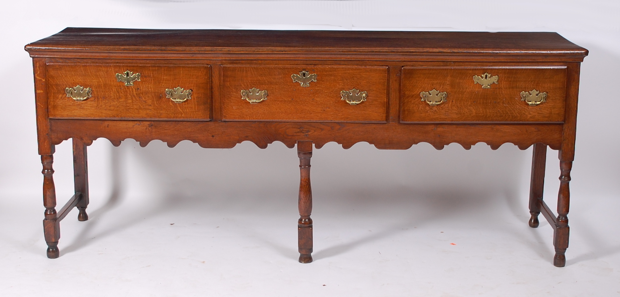 An oak dresser base in the Georgian style, having an arrangement of three frieze drawers with