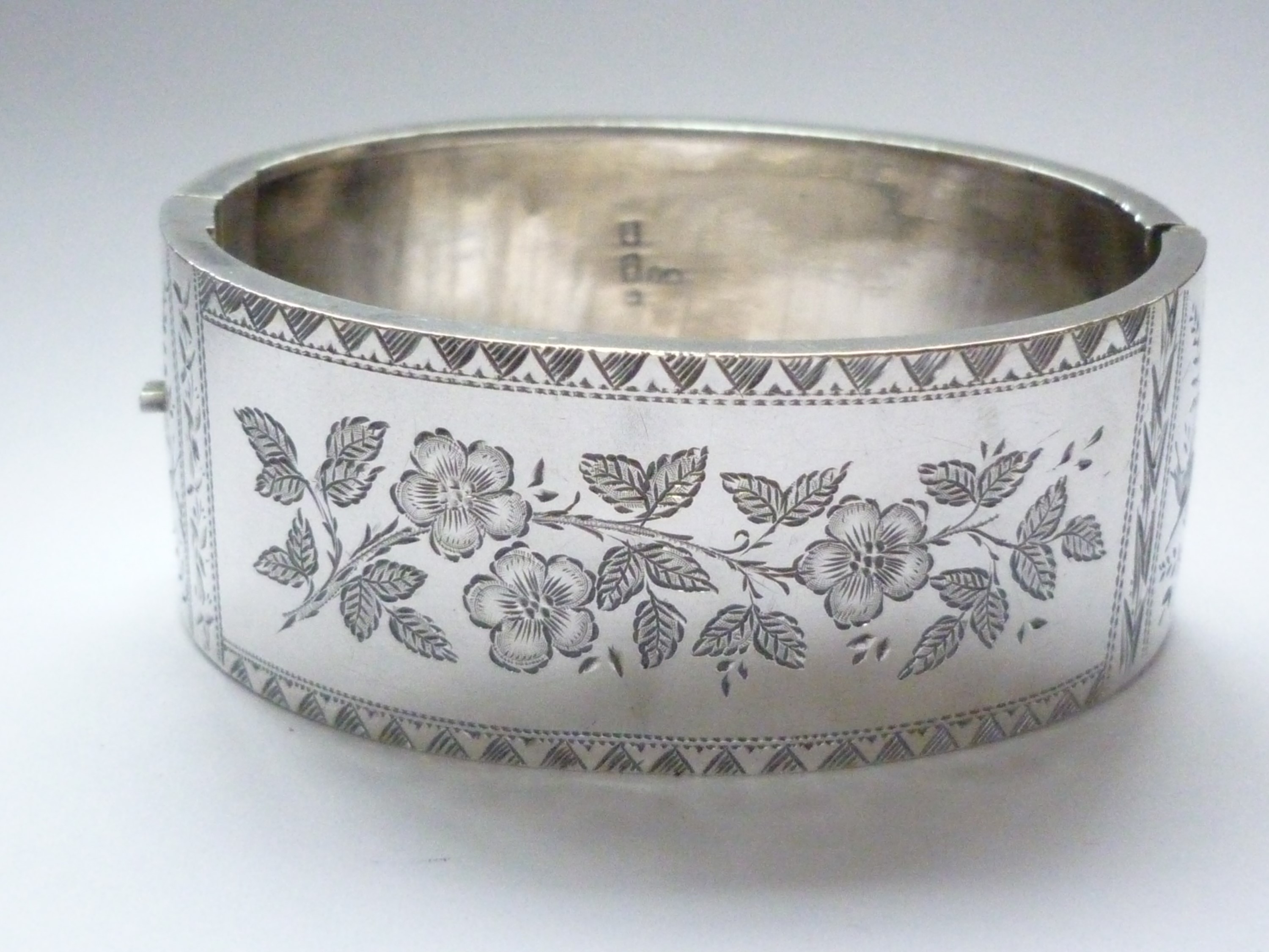 A Victorian Aesthetic Movement silver hinged-bangle, the face engraved with a floral sprig, and