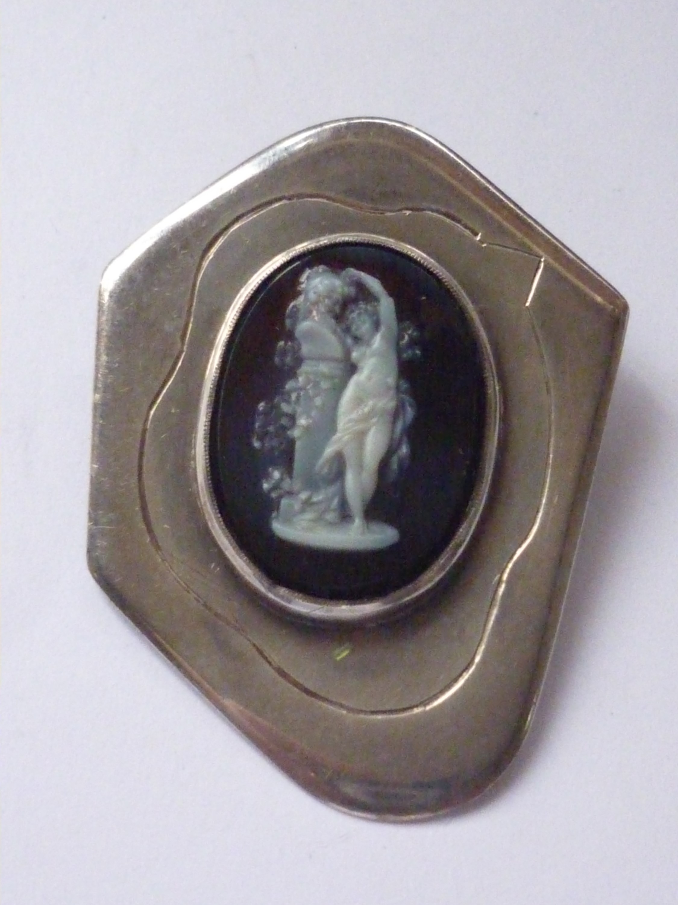 A vintage white metal and glass cameo brooch, depicting a classical figure embracing a bust on a