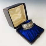 An Edwardian silver napkin ring in a fitted presentation case, the napkin ring having repousse