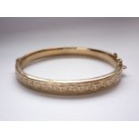 A 9ct gold hinged bangle, decorated with engraved foliage to the face, 10.2g