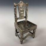 A continental white-metal miniature chair, repousse decorated with a young maiden to the back splat,