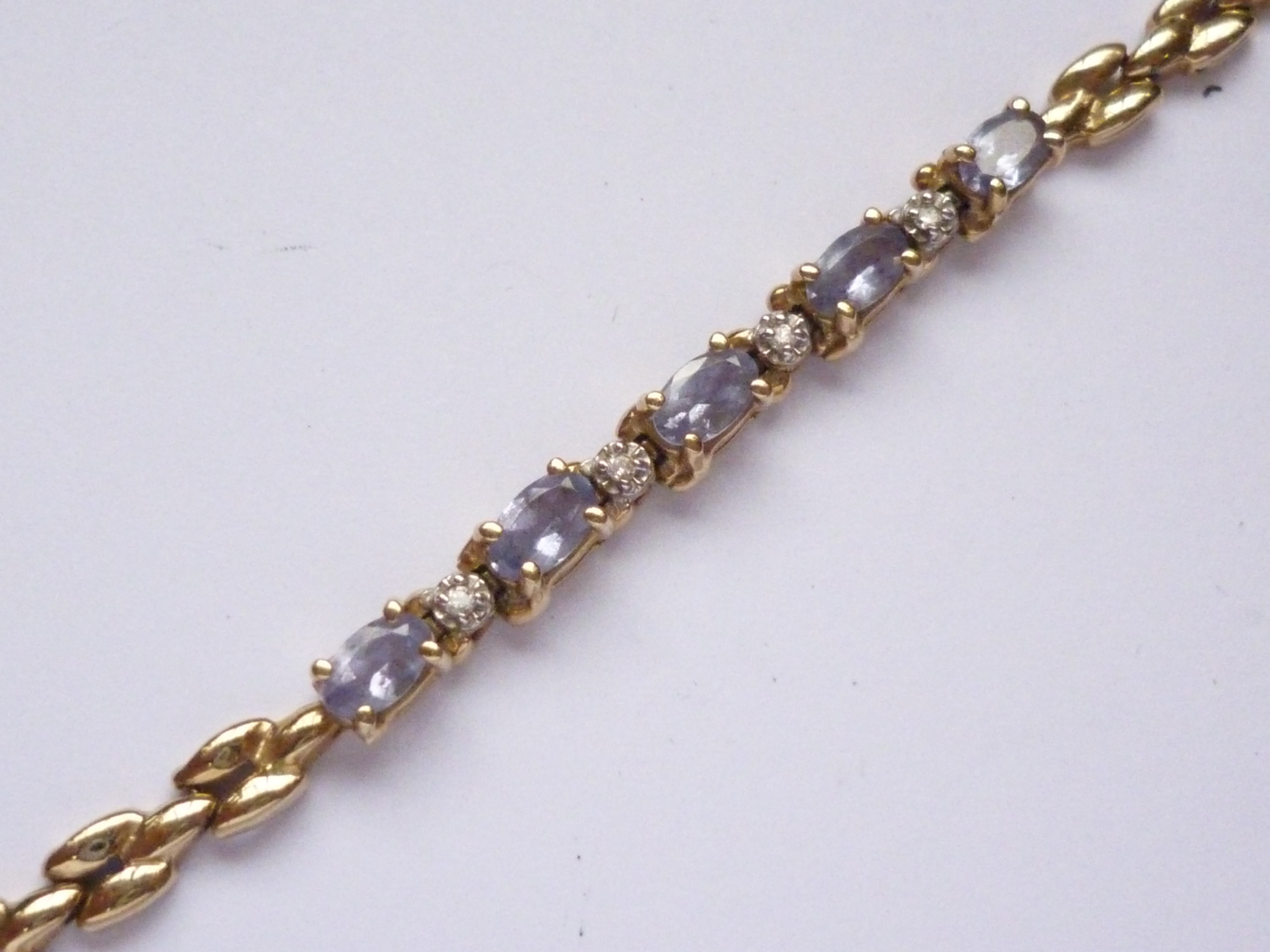 A high carat yellow-metal, diamond and tanzanite bracelet, having five oval-cut and claw set