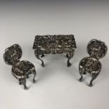 An Edwardian silver miniature table and chairs, repousse moulded with vignettes of cherubim, Levi