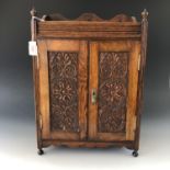 A Victorian stained oak wall mounting smokers cabinet, having a pair of doors with chip carved