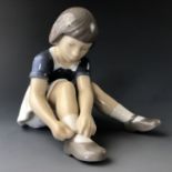 A Royal Copenhagen figurine of a girl fastening her shoe, 2317, 10 cm (a/f)