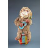 A mid-20th Century Nomura Toys of Japan clockwork toy monkey playing a tinplate guitar, seated