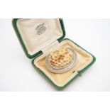 A Victorian carved ivory brooch, depicting a bed of roses, in a white metal frame of antique