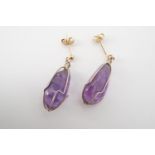 A contemporary pair of amethyst and yellow metal ear pendants, each having a captive amethyst