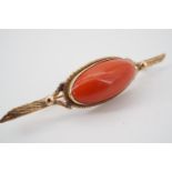 A high carat yellow metal and coral bar brooch, with central lenticular cabochon of approximately