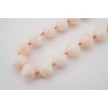 A peach jade polished bead necklace with high carat yellow metal clasp, stamped 'K18', 61 cm in