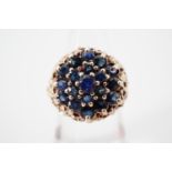 An early 1970s sapphire cocktail ring, claw-set in a tiered flower head cluster arrangement, with