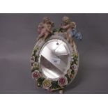 Late 19th Century Continental porcelain oval table mirror mounted with roses and figures of cherubs,