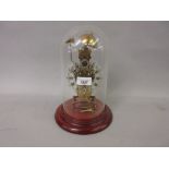 Reproduction brass skeleton clock housed under a glass dome on a circular mahogany