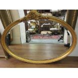 20th Century oval gilt framed wall mirror with floral surmount, 27.5ins high x 37ins