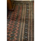 Pakistan rug of Bokhara design with six rows of gols on a salmon pink ground with borders, 10ft x