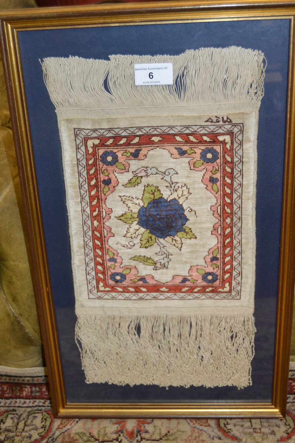 Small modern sample rug with floral design on a beige ground mounted in a gilt frame, signed
