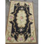 Small Aubusson type needlepoint rug with floral design on a black ground, 59ins x 36ins